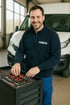 Ein lächelnder Mann in IVECO-Jacke nimmt Werkzeuge aus einem Werkzeugkasten, mit einem weißen Transporter im Hintergrund.
