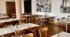 Leeres Restaurant mit Holztischen, Stühlen, weißer Tischwäsche und Wandbildern.