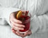 Hände in weißem Zopfstrickpullover halten ein Glas mit rotem Glühwein, garniert mit Orange, Zimt und Sternanis.