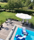Eine erhöhte Ansicht einer Holzterrasse mit Pool, Gartenmöbeln, Sonnenschirm und aufblasbaren Liegen im Pool.