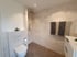Modernes Badezimmer mit Toilette, Dusche, cremefarbenen Fliesen und zwei Handtüchern.