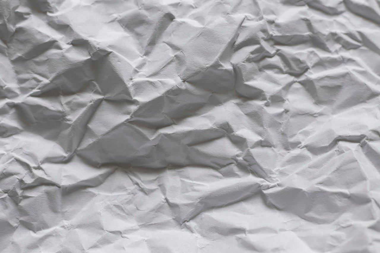 Ein grau zerknittertes Blatt Papier mit tiefen Falten und Schatten