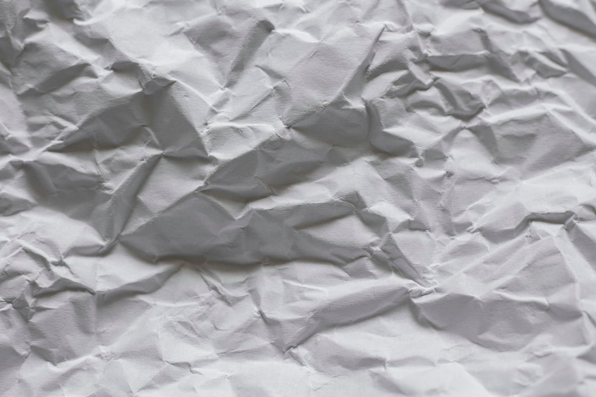 Ein grau zerknittertes Blatt Papier mit tiefen Falten und Schatten