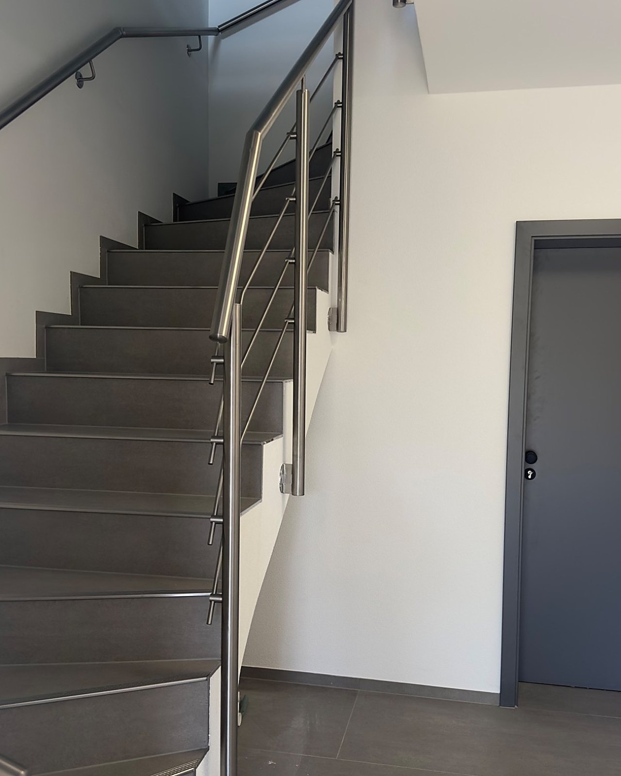 Modernes Treppenhaus mit grauen Stufen und Edelstahlgeländer.
