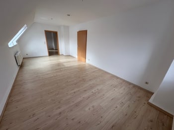 Leeres Zimmer unter der Dachschräge mit einem Fenster und Heizkörper