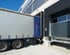 Ein LKW mit weißem Auflieger parkt rückwärts an einer Laderampe eines Logistikzentrums mit Sektionaltor.
