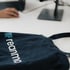 Dunkelblaue Stofftasche mit dem weißen Logo „reanmo“ und blauen Pfeilen, auf weißem Schreibtisch.