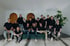 Eine Gruppe von 18 Personen in dunklen T-Shirts und Kapuzenpullis posiert in einem modernen Raum.