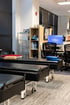 A physical therapy clinic featuring rows of black padded treatment tables on wheels, office desks, and a computer monitor.