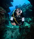 Ein Taucher im Neoprenanzug mit Tauchermaske und Atemregler schwimmt in einer Unterwasserhöhle.