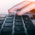 Ein Finger drückt die Enter-Taste auf einer schwarzen Laptop-Tastatur.
