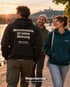 Drei Menschen am Flussufer im Abendlicht, vorne ein dunkler Wearmorrow® Hoodie mit der Rückenbotschaft Menschenwürde ist keine Meinung