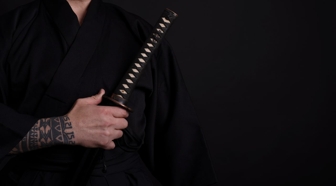 Hände in schwarzer Kampfkunst-Kleidung halten ein Katana
