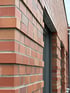 Rote Klinkerfassade mit horizontal versetzten Ziegelreihen und einem dunklen Fensterrahmen.