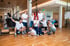 Ein lächelndes Physiotherapie-Team posiert mit Trainingsgeräten wie Faszienrollen und Bällen in einem modernen Fitnessstudio.