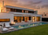 Modernes Haus mit Pool, Terrasse und Garten bei Sonnenuntergang.