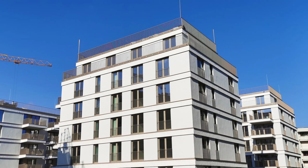 Modernes weißes Apartmentgebäude mit Balkonen, vielen Fenstern und Solarpaneelen auf dem Dach unter blauem Himmel.