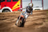 Ein Motocross-Fahrer auf einer orangefarbenen Maschine mit der Nummer 98 fährt auf einer Sandpiste.
