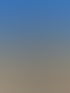 Eine Frau mit langem Haar, Jeans und Weste umarmt ein braunes Pferd auf einem Kiesplatz unter blauem Himmel.