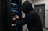 Person mit Kapuzenpullover arbeitet an Server-Rack mit blauen Kabeln in einem Serverraum - Software-KRITIS Notfall- und Krisenmanager (NKM®).