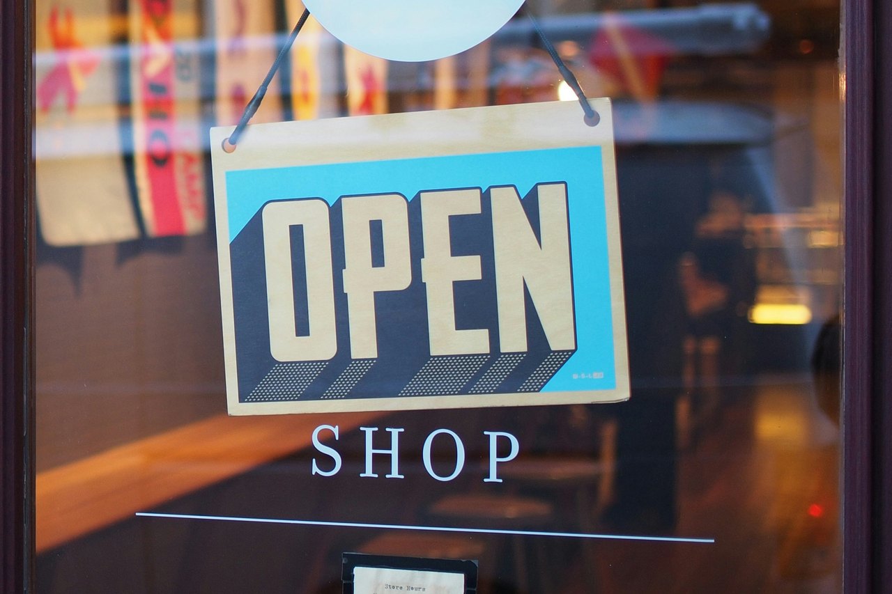 Ein Schild mit der Aufschrift OPEN hängt an einer Glastür mit dem Schriftzug SHOP.
