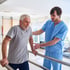 Male physical therapist assists a senior man using parallel bars for rehabilitation.