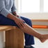 A man sits on a wooden bench while holding his leg and calf muscle.