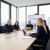 Fünf Personen sitzen um einen Tisch in einem Konferenzraum; auf dem Bildschirm steht „WORKPLACE SAFETY FIRST INITIATIVE“.