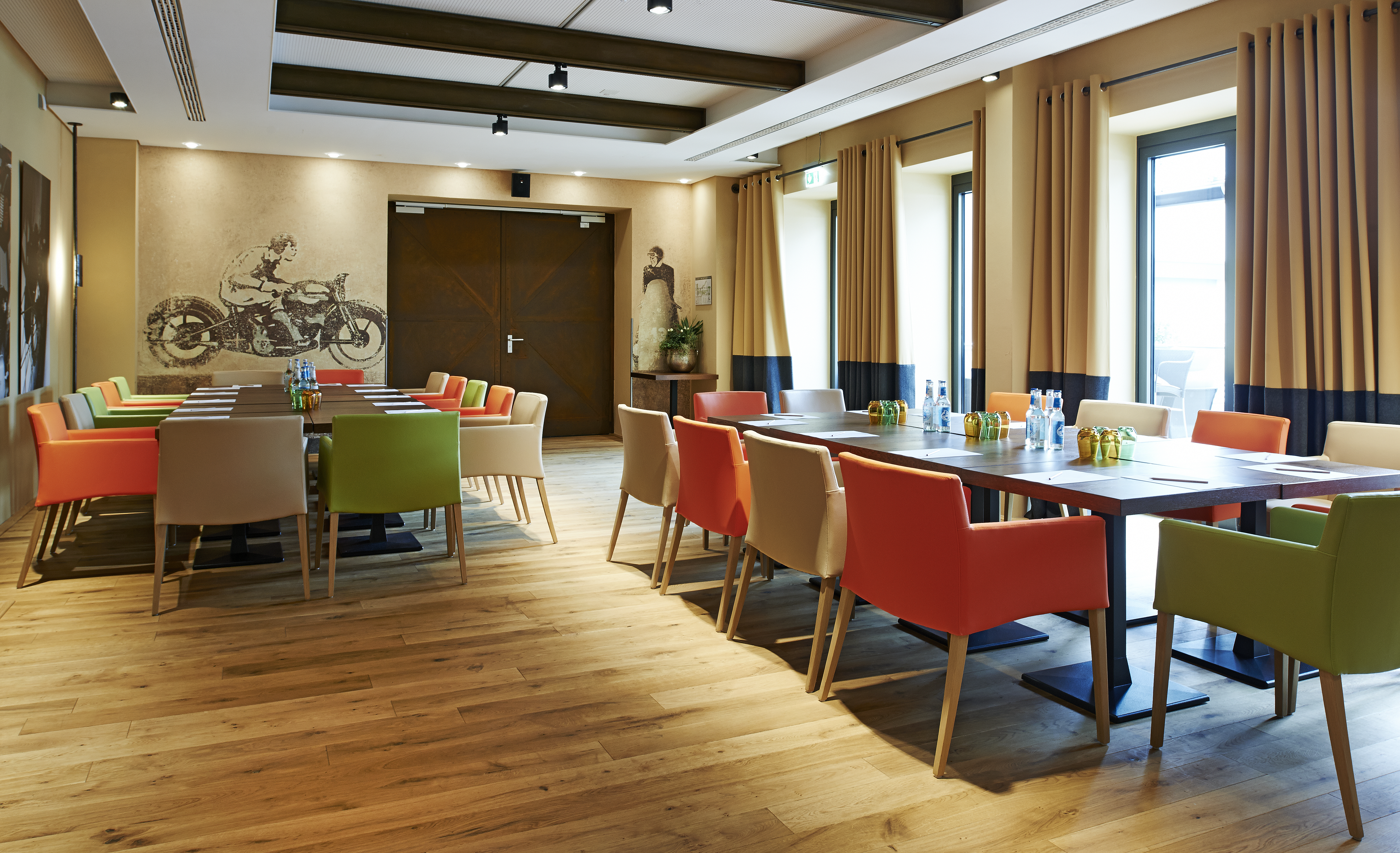 Heller Veranstaltungsraum mit Holzboden und farbigen Stühlen