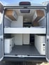 Innenraum eines Campervans mit festem Querbett, Oberschränken und Stauraum im Heck – durchdachter Grundriss für komfortables und autarkes Reisen