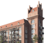 Mehrstöckiges Backsteingebäude mit Balkonen, Satteldach und einem markanten Eckturm mit Zinnen vor schwarzem Hintergrund.