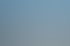 Eine DJI Drohne mit vier Rotoren schwebt über unscharfen Gebäuden vor blauem Himmel.