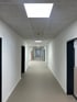 Langer, leerer Büroflur mit weißen Wänden, grauer Decke mit LED-Panels und dunklen Türrahmen.