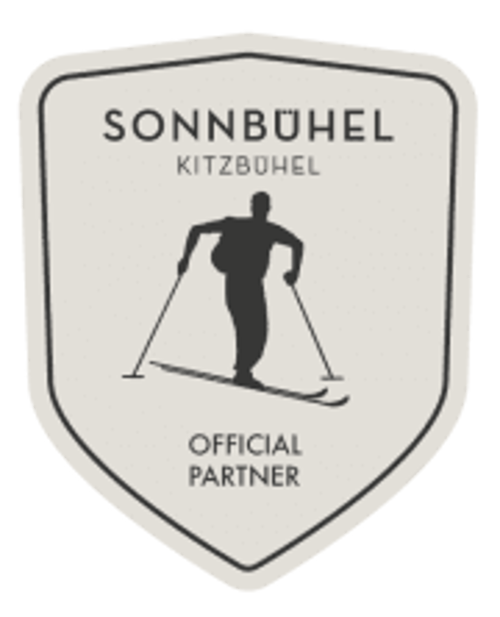 Beiges Wappen-Logo mit schwarzem Skifahrer, Text "SONNBÜHEL KITZBÜHEL OFFICIAL PARTNER".