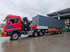 Roter Lastwagen mit Kran und einem großen, grauen Schiffscontainer auf einem Anhänger, geparkt auf nassem Asphalt.