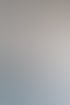 Frau sitzt an einem Holzschreibtisch in einem modernen Büro mit Glasfront und verchromter Deckenleuchte.