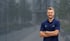 Lachender Mann im blauem Poloshirt mit gekreuzten Armen vor einem modernen Gebäude.