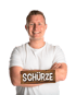 Lächelnder Mann im weißen T-Shirt mit verschränkten Armen und einem Holzschild mit der Aufschrift Schürze vor schwarzem Grund.