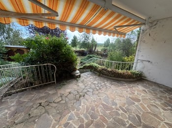Terrasse unter der gelb-weißen Markise mit Blick über die Hecke ins Grüne