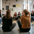 Zwei Frauen sitzen mit dem Rücken zur Kamera auf dem Boden, weitere Frauen sitzen im Kreis im Hintergrund.