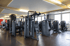 Verschiedene dunkle Krafttrainingsgeräte von Technogym stehen in einem hell beleuchteten Fitnessstudio auf dunklem Boden.