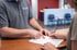 A medical center employee points to a form for a patient to sign at a reception desk.