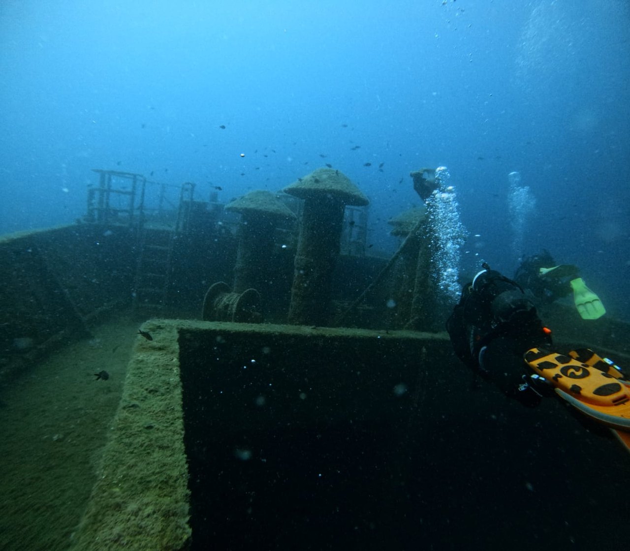 A diver with bubbles rising next to the deck of a sunken wreck