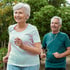 Senior woman and man jogging outdoors, enjoying exercise despite chronic pain, trees in background