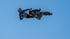 Motorradfahrer in blauer Montur und Helm fliegt seitlich mit Motorrad vor blauem Himmel