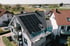 Arbeiter installiert schwarze Solarpaneele auf dem Dach eines weißen Hauses.
