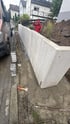 Bauarbeiter in roter Jacke errichtet eine Stützmauer aus L-Steinen aus Beton an einer Baustelle neben einer Straße.