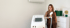 Tätowierte Frau steht lächelnd neben einem Diodenlaser-Gerät zur dauerhaften Haarentfernung in einem Behandlungsraum.