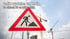 Baustellenschild mit schwarzer Figur, die eine Schaufel benutzt, vor Baukränen und bewölktem Himmel.