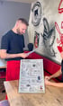 Mann in schwarzem Hemd und roter Schürze hält ein Burger-Menü in einem Restaurant.